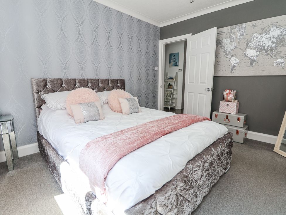 A bedroom with a bed with pink cushions and a pink throw a world map on the wall and stacked boxes at 67 Pendre Avenue in Prestatyn