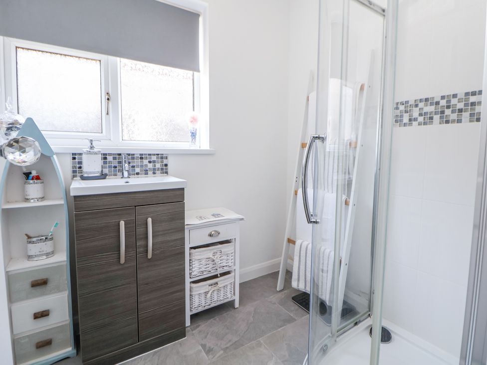 A bathroom with a shower enclosure, a sink cabinet, a small white storage unit, a towel rack ladder, and a frosted window at 67 Pendre Avenue in Prestatyn
