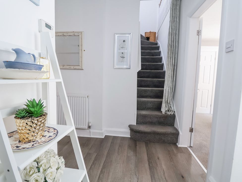 A hallway with wooden flooring a white shelf stairway with dark carpet and a doorway at 67 Pendre Avenue in Prestatyn