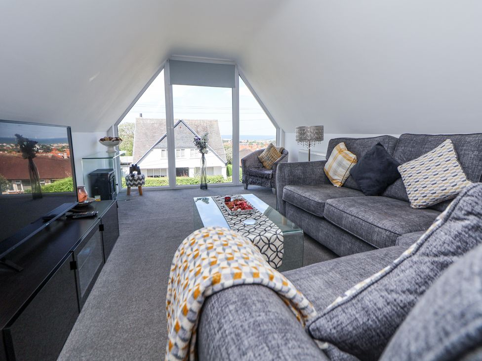 A living room with grey sofas glass coffee table and large window showing house outside at 67 Pendre Avenue in Prestatyn