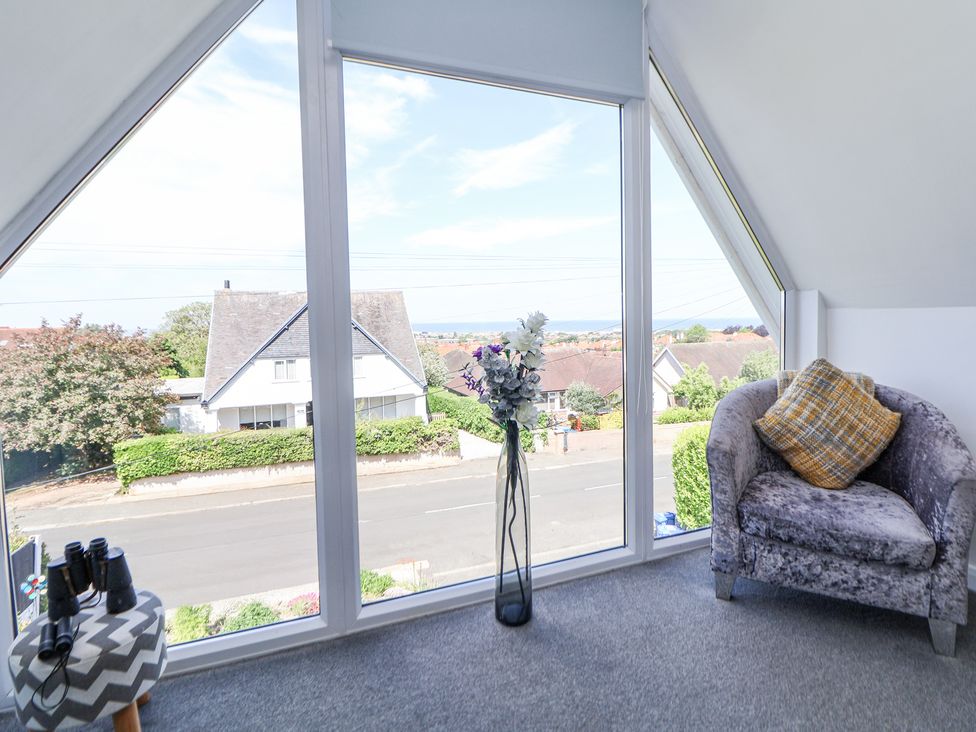 A seating area with a chair and a small table with binoculars by a large window showing a street and houses at 67 Pendre Avenue in Prestatyn