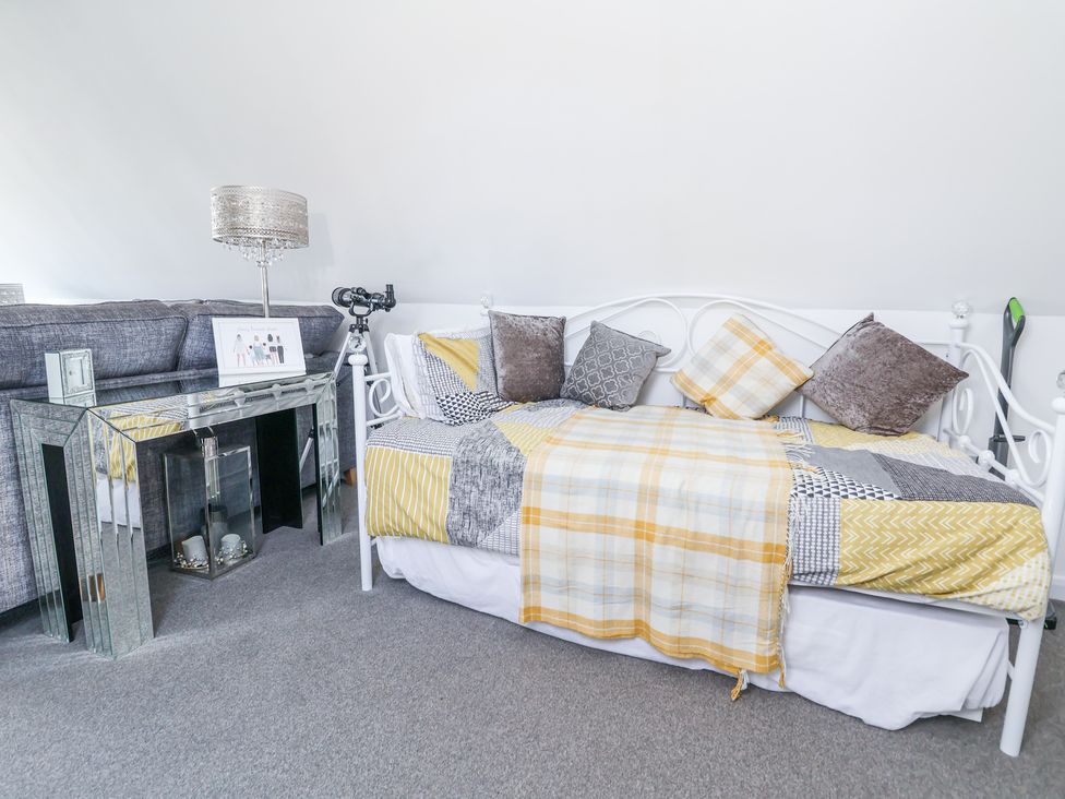 A room with a white daybed with cushions and a yellow patterned blanket next to a mirrored console table with a lamp and telescope at 67 Pendre Avenue in Prestatyn