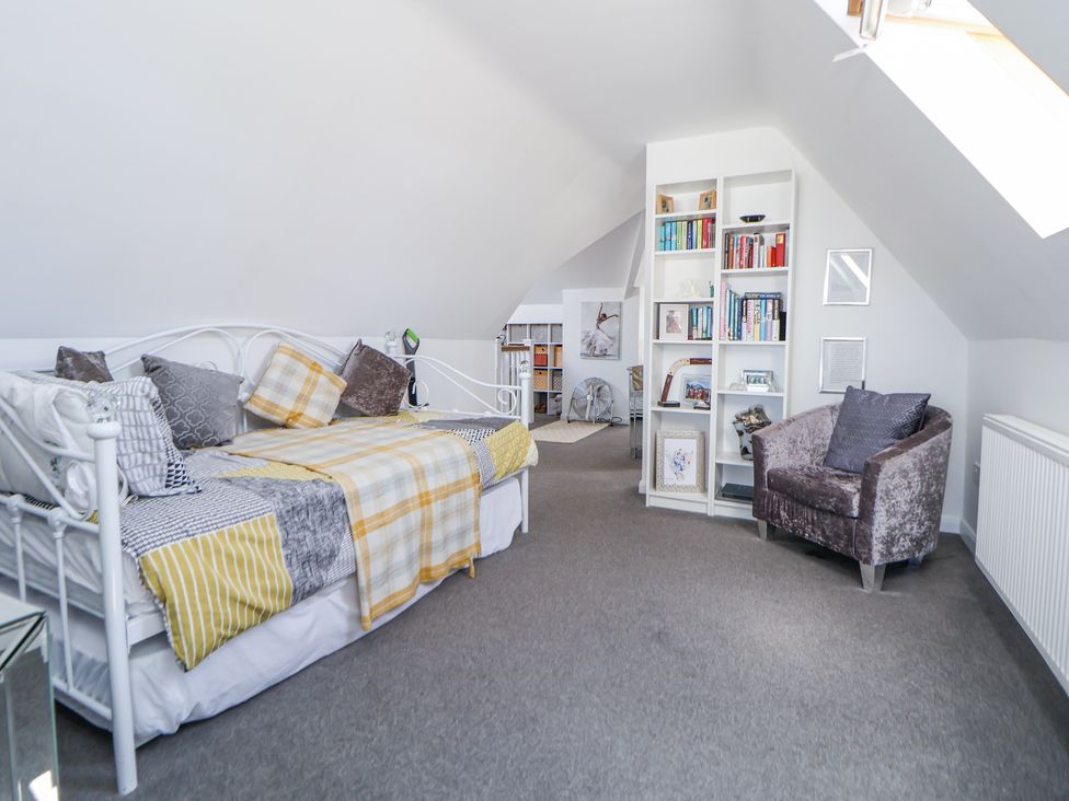 A bedroom with a white metal-framed bed with pillows and a blanket a bookshelf and a velvet armchair at 67 Pendre Avenue in Prestatyn