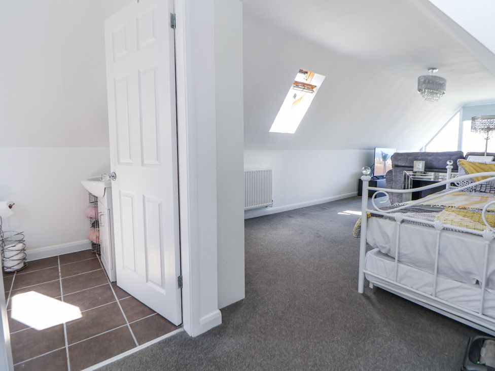 A bedroom with a white metal bed frame and a gray sofa in the background with a skylight window in the ceiling and an open door leading to a bathroom at 67 Pendre Avenue in Prestatyn