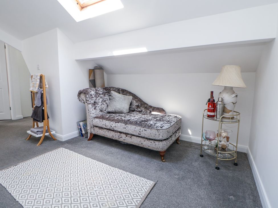A room with a chaise lounge pillow and a small table with a lamp and bottles at 67 Pendre Avenue in Prestatyn