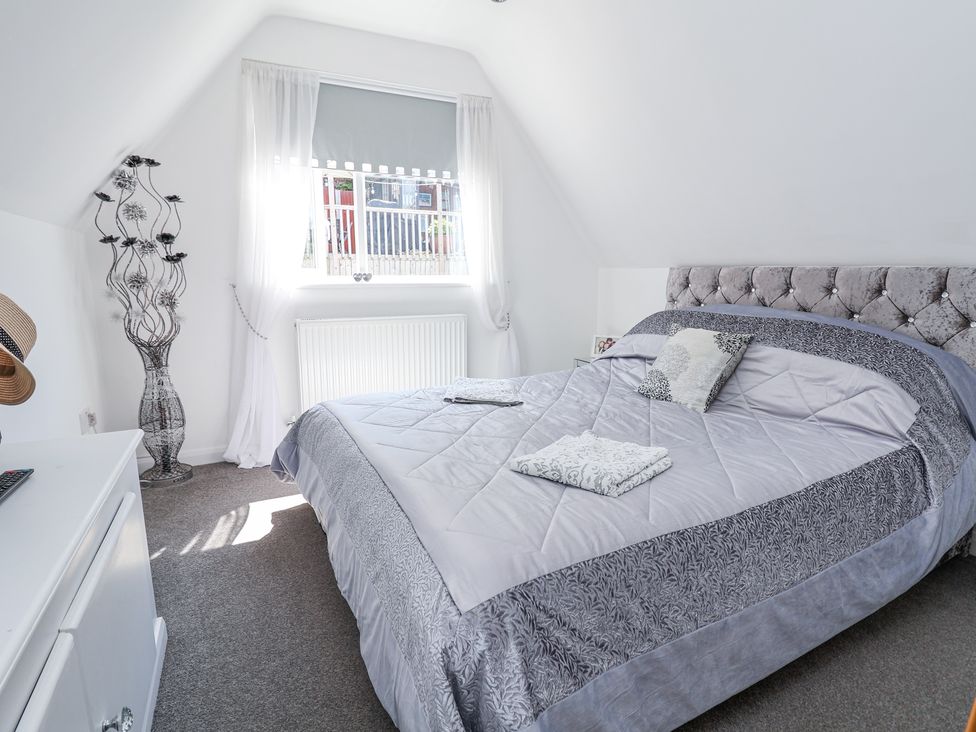 A bedroom with a large bed with folded towels on it a window with curtains a decorative vase and a small cabinet at 67 Pendre Avenue in Prestatyn