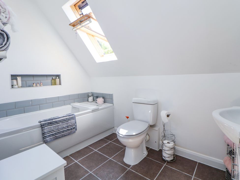 A bathroom with a bathtub a toilet a skylight window and tiled floor at 67 Pendre Avenue in Prestatyn
