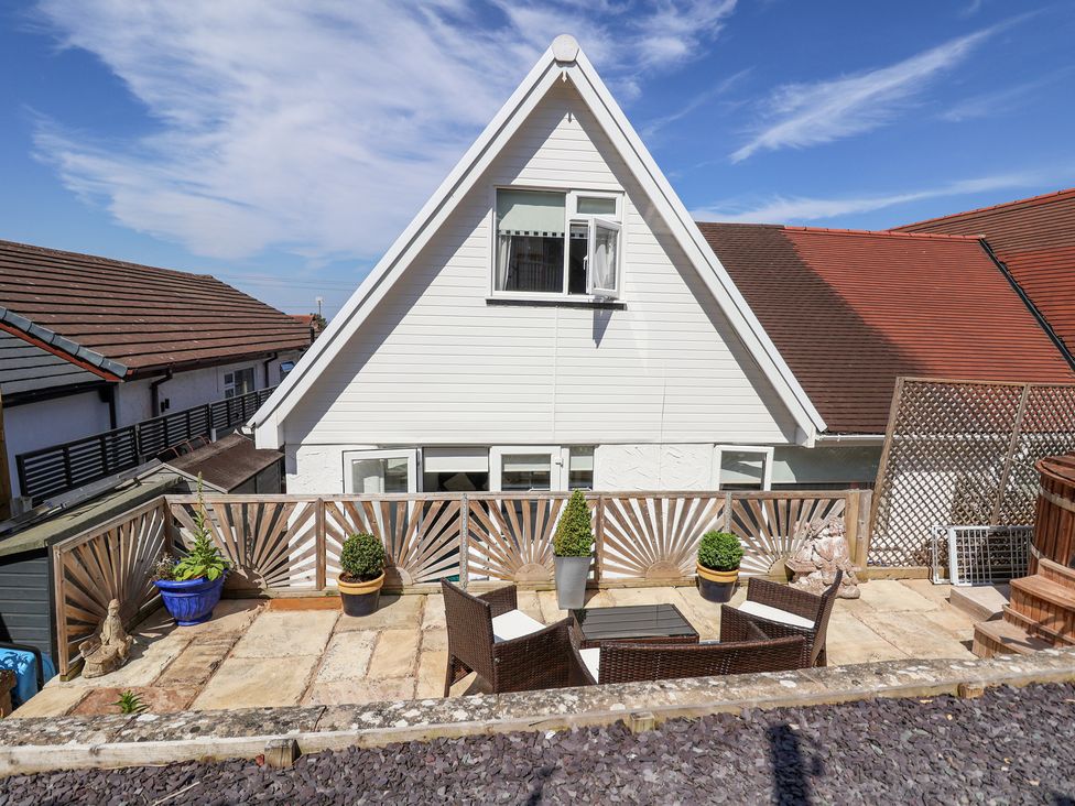 An outdoor patio area with a wooden fence table chairs potted plants and statues in front of a white house with a triangular roof at 67 Pendre Avenue in Prestatyn