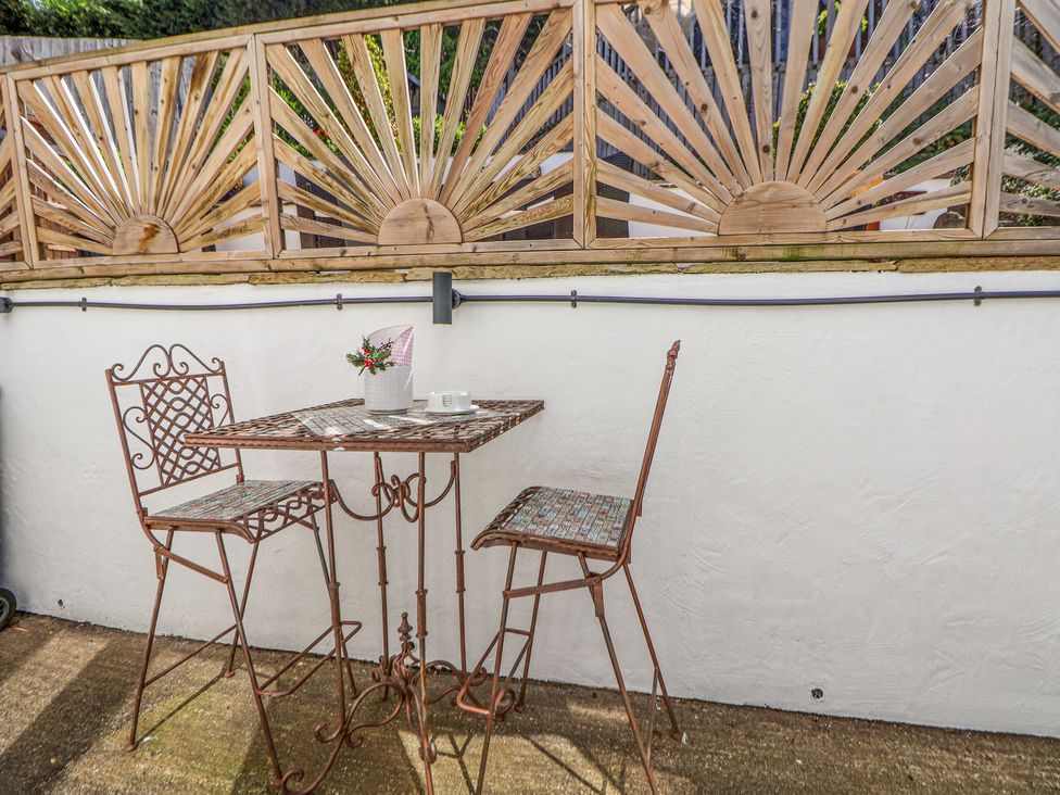 An outdoor seating area with a metal table and two chairs against a white wall with wooden sunburst fence at 67 Pendre Avenue in Prestatyn