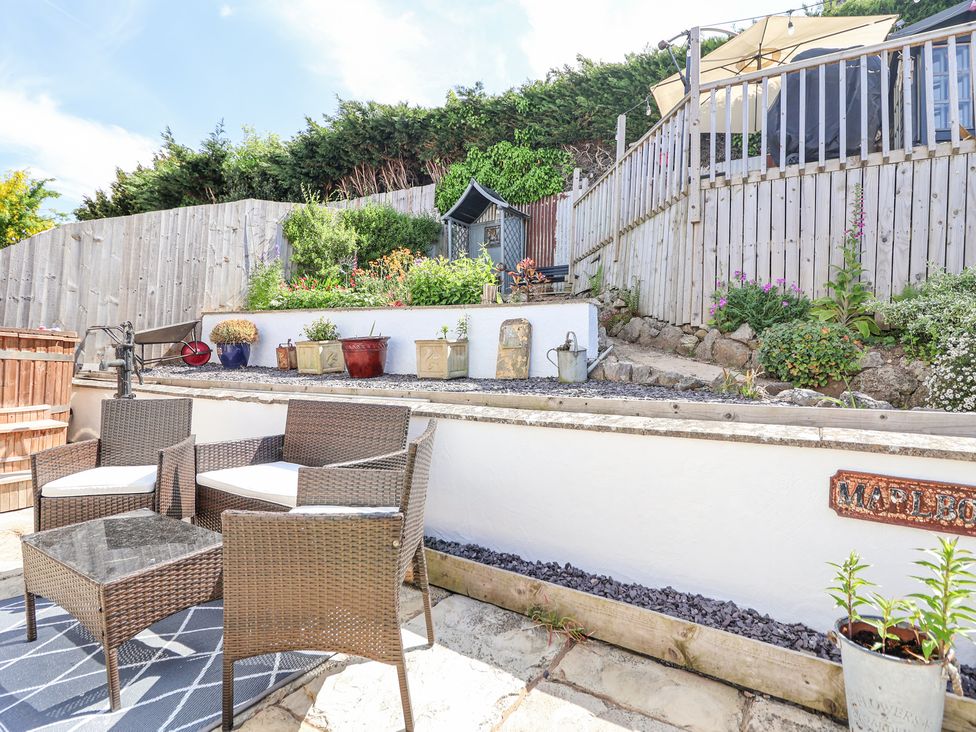An outdoor patio area with wicker chairs and a table with potted plants and a wooden fence in the background at 67 Pendre Avenue Prestatyn