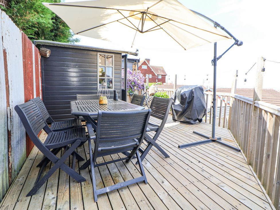 A wooden deck with black outdoor furniture and a large umbrella at 67 Pendre Avenue in Prestatyn
