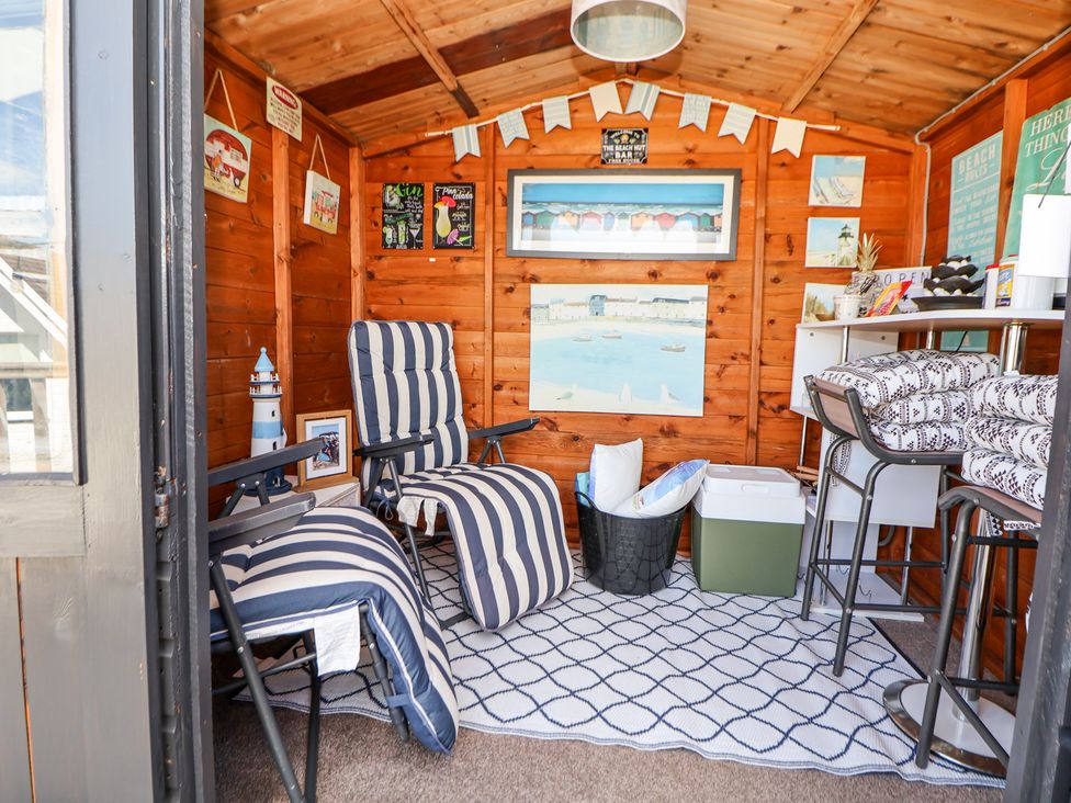 A wooden shed interior with striped reclining chairs a rug bar stools wall art and various decorations at 67 Pendre Avenue in Prestatyn