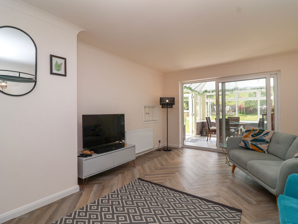 A living room with a TV on a stand a patterned rug a sofa with cushions sliding doors to a conservatory at Hillside in Bishops Cleeve