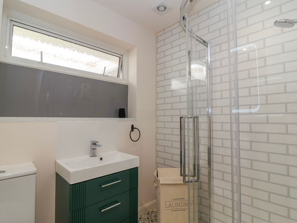 A bathroom with a green vanity and sink a toilet a laundry basket a glass shower enclosure and a frosted window at Hillside in Bishops Cleeve