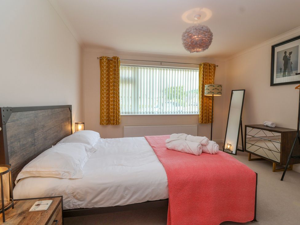 A bedroom with a bed with white sheets and a coral blanket at Hillside in Bishops Cleeve