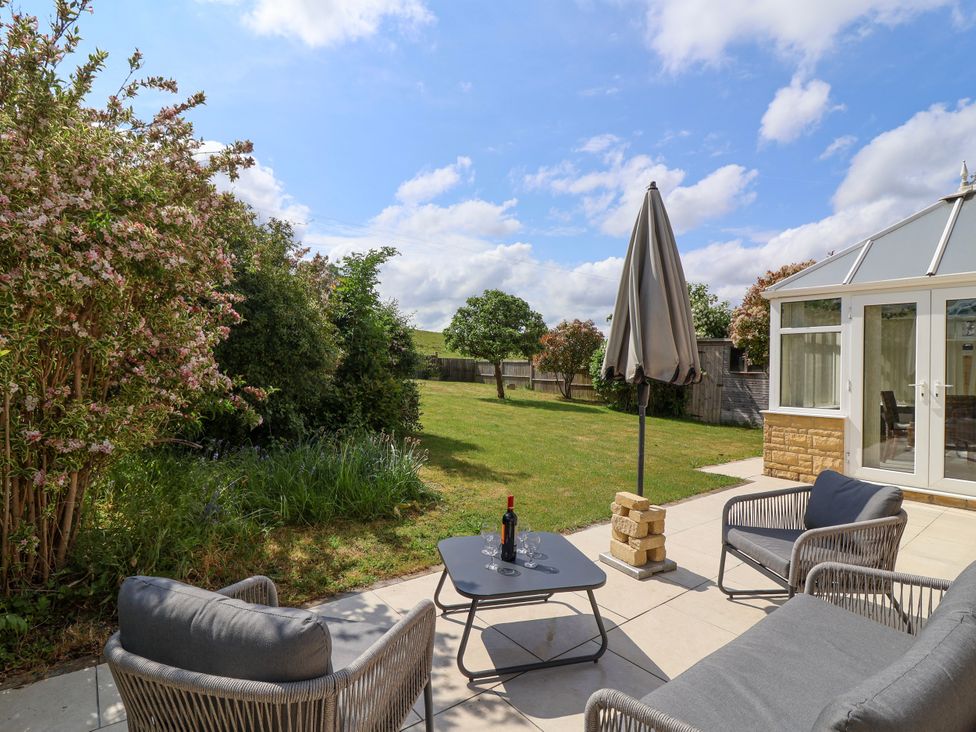 A garden patio with outdoor seating and a table with wine at Hillside in Bishops Cleeve