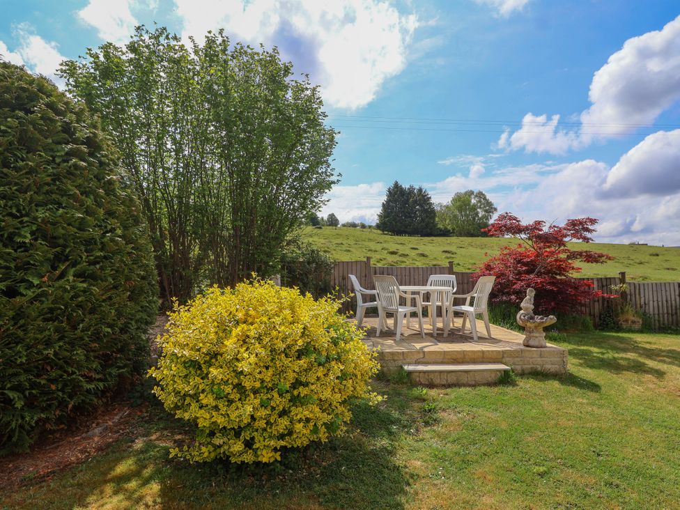 An outdoor patio area with plastic chairs and table surrounded by bushes and grass at Hillside in Bishops Cleeve