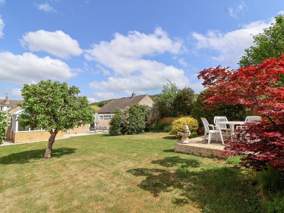 A garden with a tree a patio with white chairs and table a house in the background at Hillside in Bishops Cleeve
