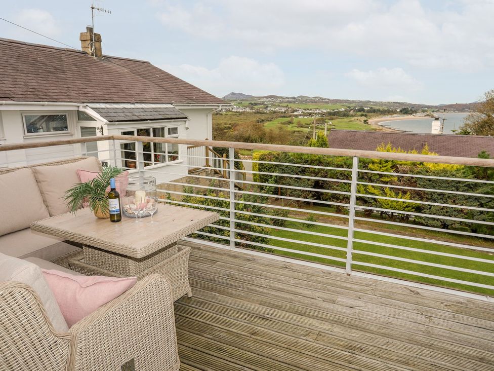 A deck area with a couch and table overlooking the landscape at Machroes Cottage Pwllheli
