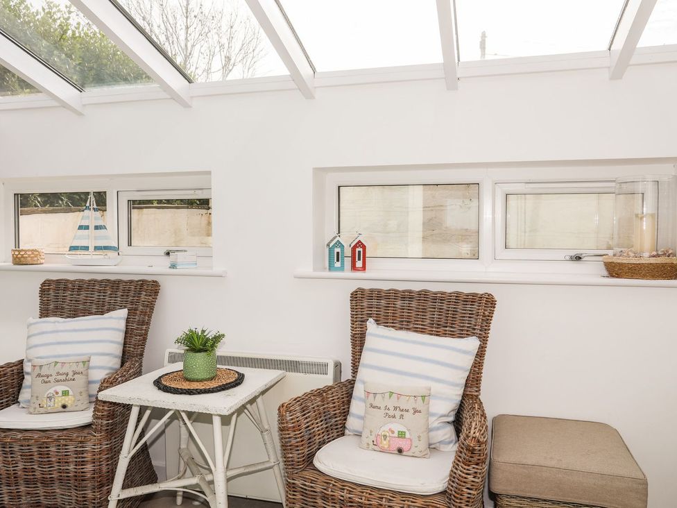 A conservatory with armchairs and a table at Machroes Cottage in Pwllheli