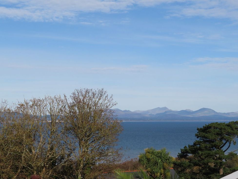 A view of the sea and mountains with trees at Machroes Cottage Pwllheli