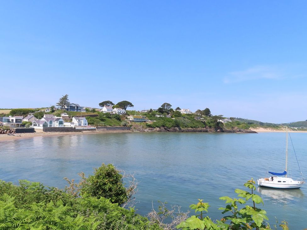 A view of houses near the shore with a boat on the water at Machroes Cottage Pwllheli