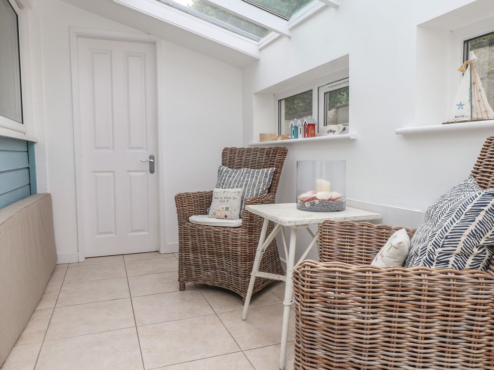 A conservatory with rattan chairs and a table at Machroes Cottage near Bwlchtocyn
