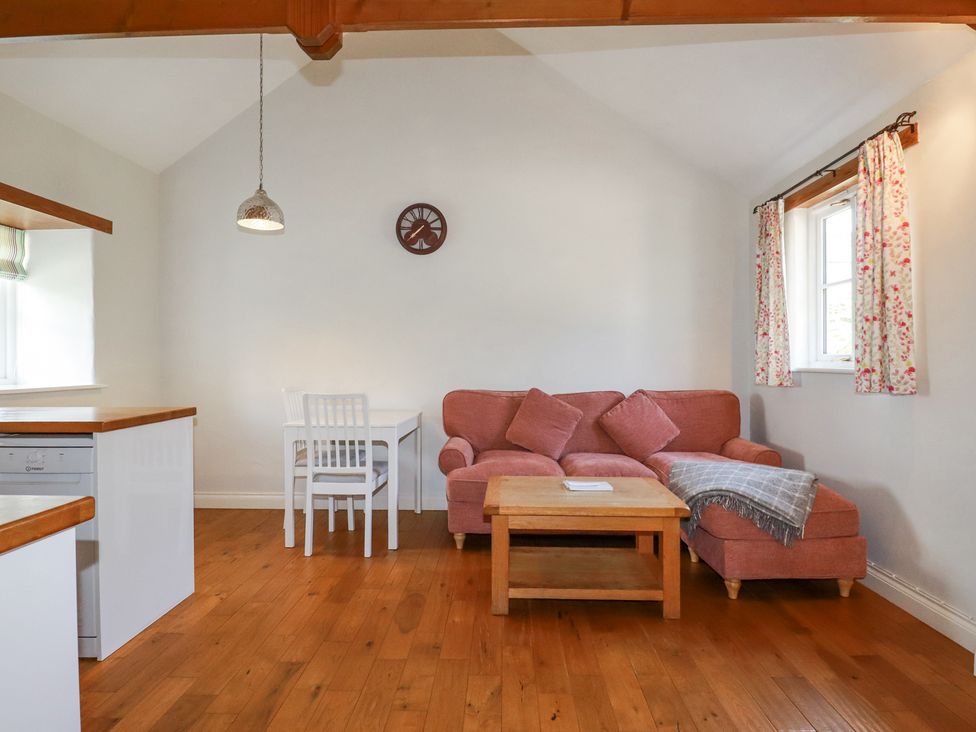A living room with a pink sofa a wooden coffee table a white dining table with two chairs and floral curtains at Rose's Stable in Bodrean near Truro
