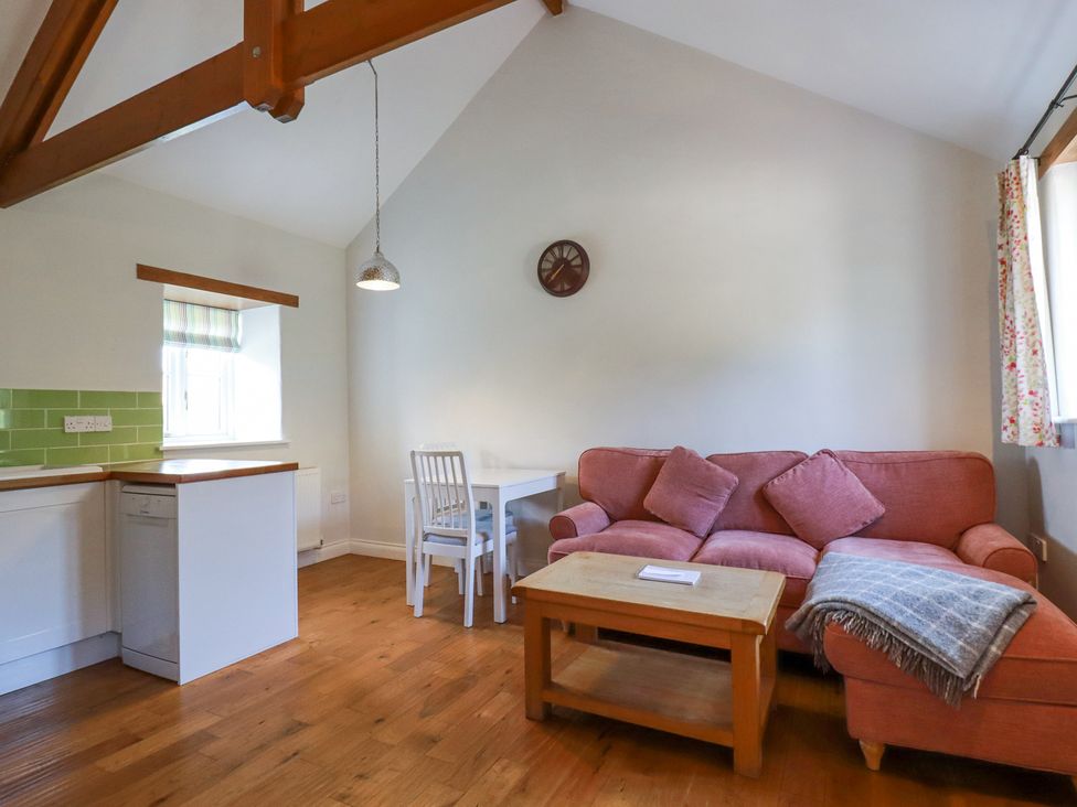 A living area with a pink sofa a wooden coffee table white dining table and chairs and a kitchen corner at Roses Stable Bodrean near Truro