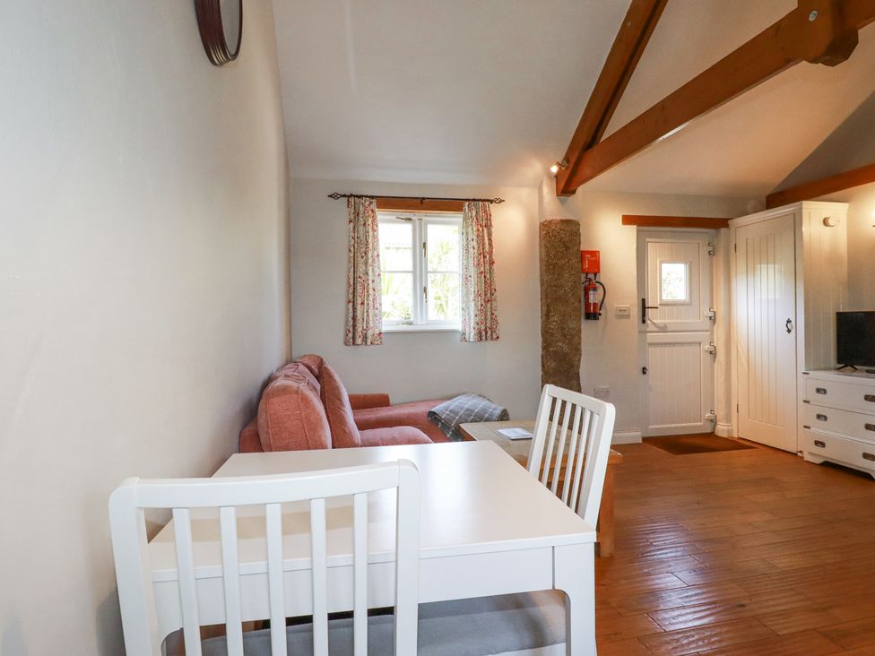 A living room with a white dining table and chairs a pink sofa floral curtains a wooden floor and a white door at Rose's Stable Bodrean near Truro