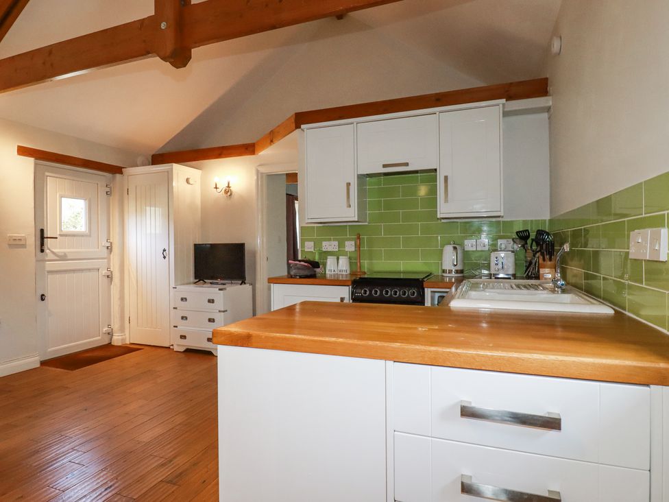 A kitchen with wooden countertops white cabinets green tiled backsplash and a small television at Rose's Stable Bodrean near Truro