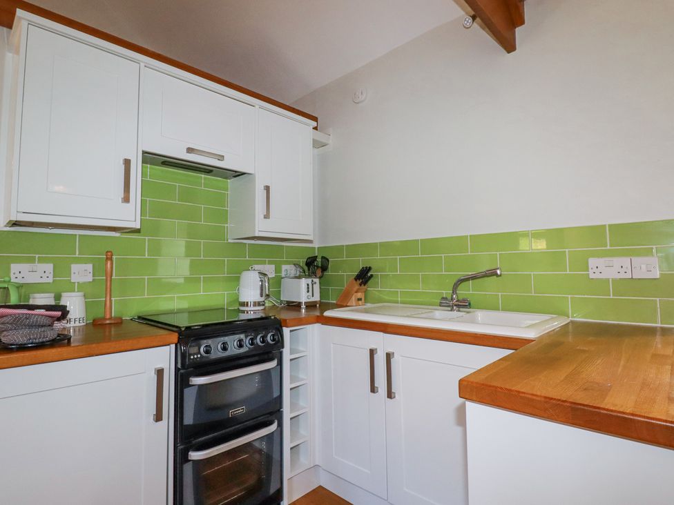 A kitchen with white cabinets green tiled backsplash a black stove a white sink and wooden countertops at Roses Stable Bodrean near Truro