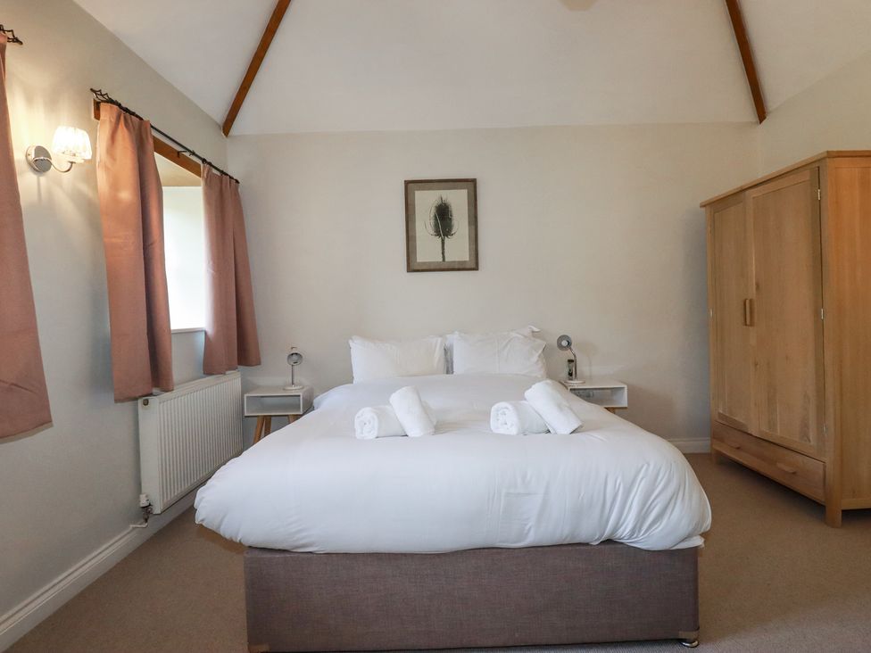 A bedroom with a bed with white linens and towels two bedside tables with lamps a wardrobe and curtains at Rose's Stable in Bodrean near Truro