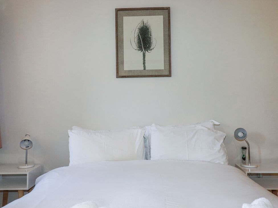A bedroom with a white bed between two nightstands with lamps and a framed botanical print above the bed at Roses Stable in Bodrean near Truro
