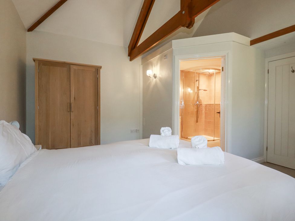 A bedroom with a wooden wardrobe and an en suite bathroom with a shower at Rose's Stable in Bodrean near Truro