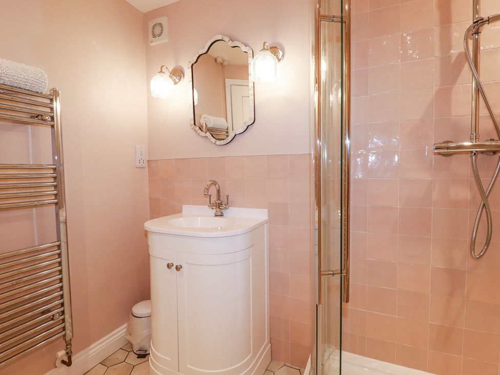 A bathroom with a white sink cabinet a mirror and wall lights beside a glass shower enclosure with a showerhead and a metal towel rack at Roses Stable in Bodrean near Truro