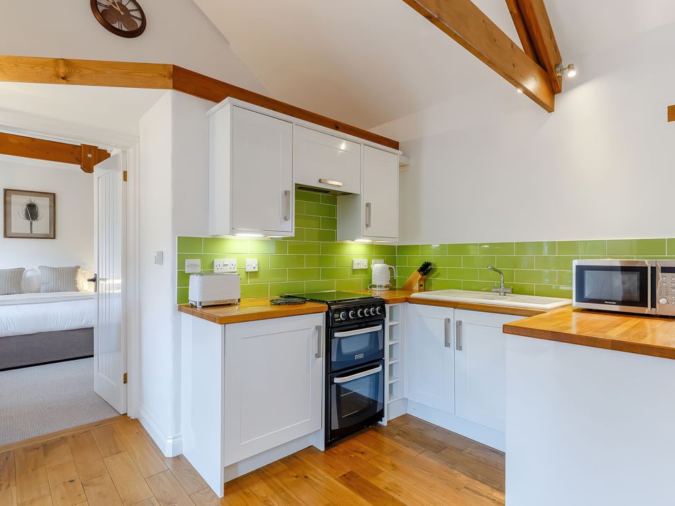 A kitchen with white cabinets wooden countertops green tile backsplash and a doorway to a bedroom at Roses Stable Bodrean near Truro