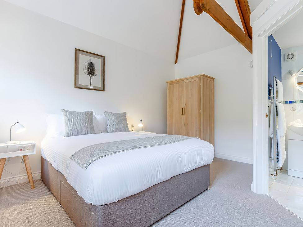 A bedroom with a double bed two bedside tables lamps a wooden wardrobe and a doorway to a bathroom at Roses Stable in Bodrean near Truro