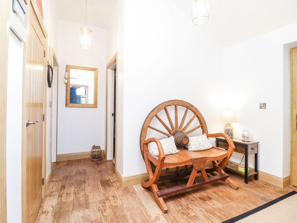 A hallway with a wooden chair and a mirror at Perth Y Deri in Llanddwywe