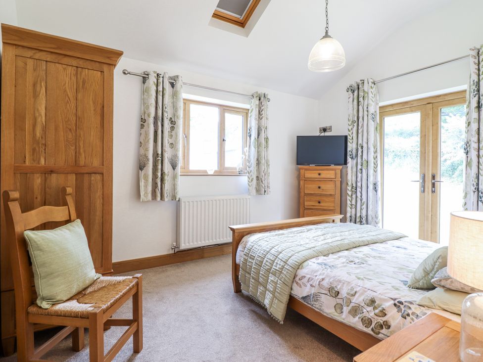 A bedroom with a bed, chair, dresser, and television at Perth Y Deri, Llanddwywe