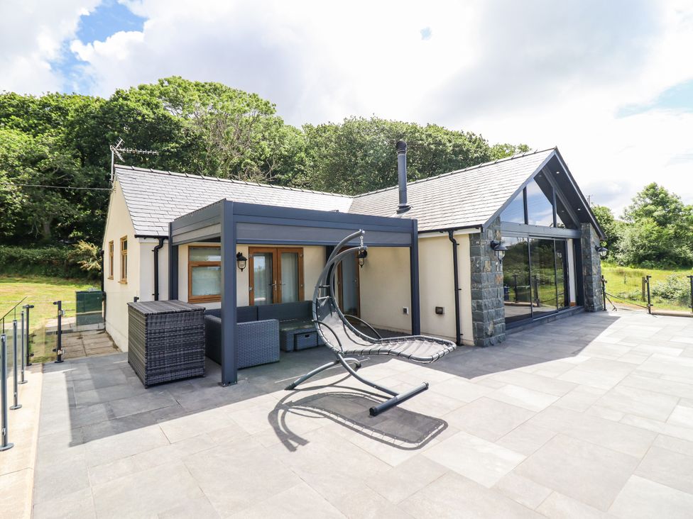 A house with a patio and swing chair at Perth Y Deri in Llanddwywe