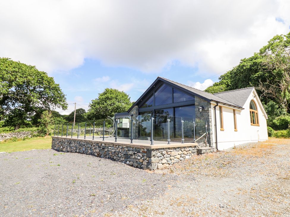 A house with glass railings and stone wall in the outdoor area at Perth Y Deri Llanddwywe