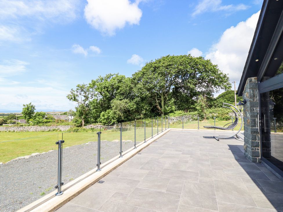 An outdoor patio with glass railing and grass at Perth Y Deri in Llanddwywe