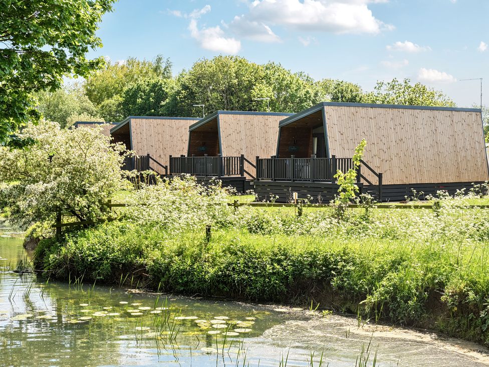 Wooden cabins beside a pond with greenery and trees at Celestial Skylight - Billing Aquadrome in Billing Aquadrome Holiday Park