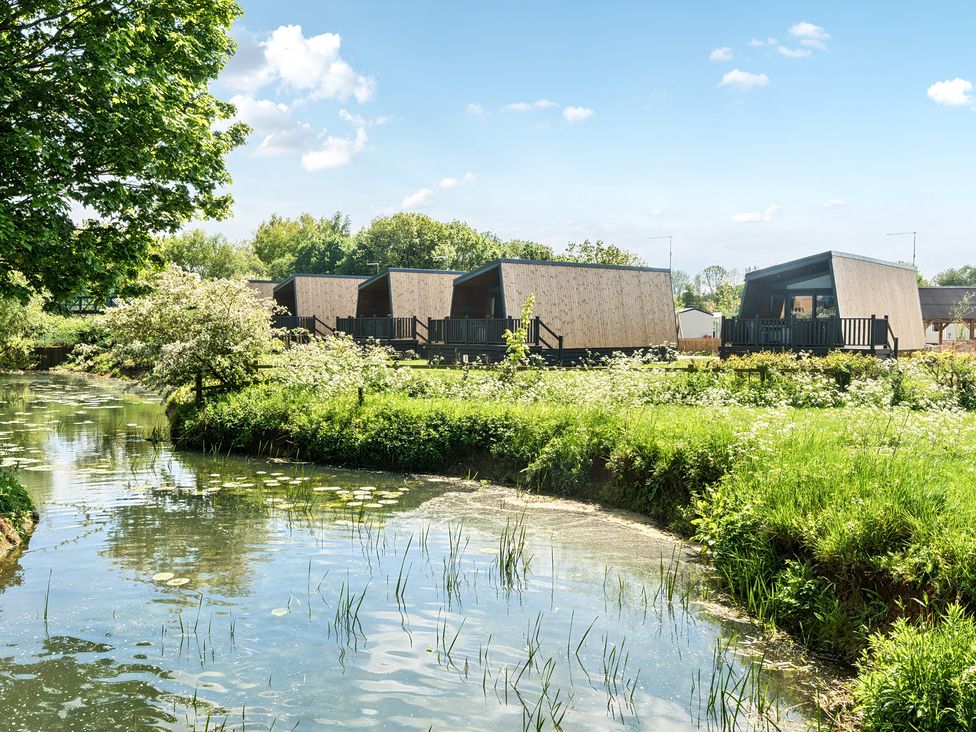 A row of modern wooden cabins near a waterway with lilies and green vegetation at Celestial Skylight - Billing Aquadrome in Billing Aquadrome Holiday Park