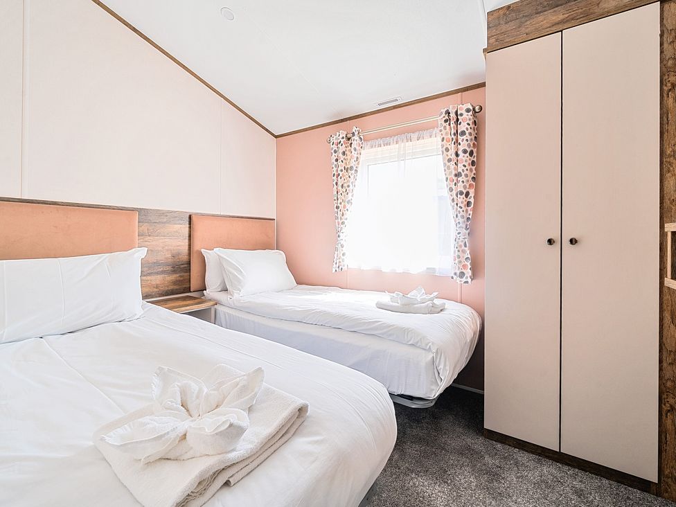 A bedroom with two single beds white bedding a double door wardrobe and a window with patterned curtains at Lakeside Lullaby - Billing Aquadrome Holiday Park