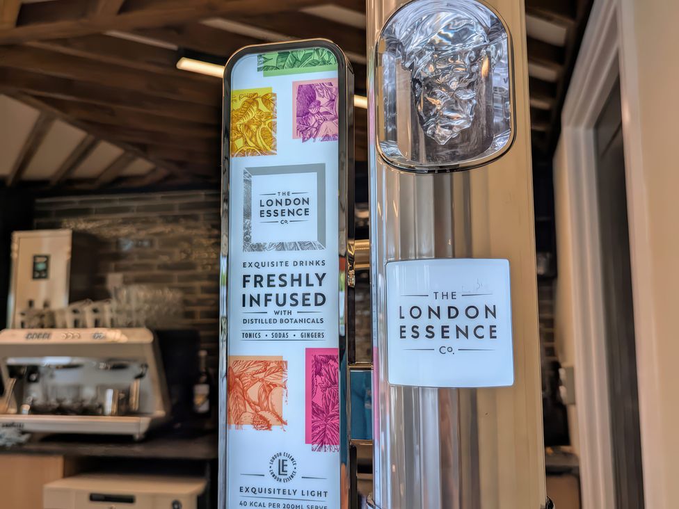 A beverage dispenser with The London Essence Co branding in a room with a brick wall and coffee machine
