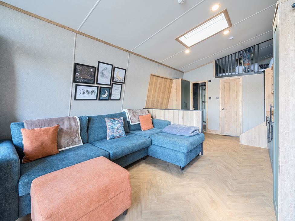 A living area with a blue sectional sofa and orange ottoman under framed wall art and a skylight at Moonlit Skylight - Billing Aquadrome in Billing Aquadrome Holiday Park