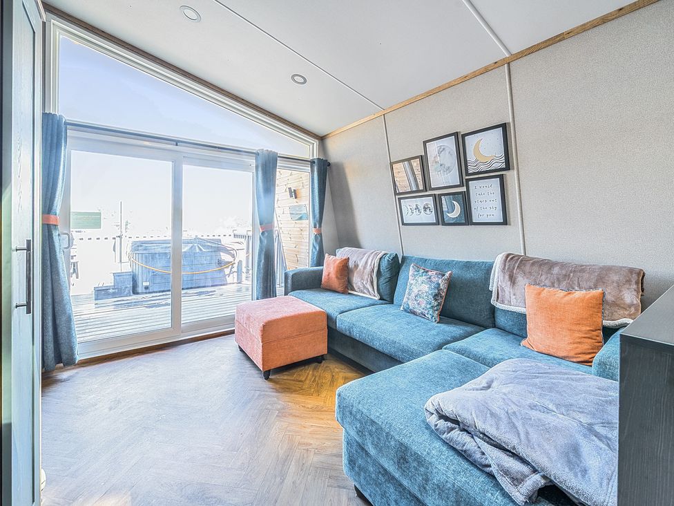 A living room with a blue sectional sofa an orange ottoman and framed pictures on the wall at Moonlit Skylight - Billing Aquadrome in Billing Aquadrome Holiday Park