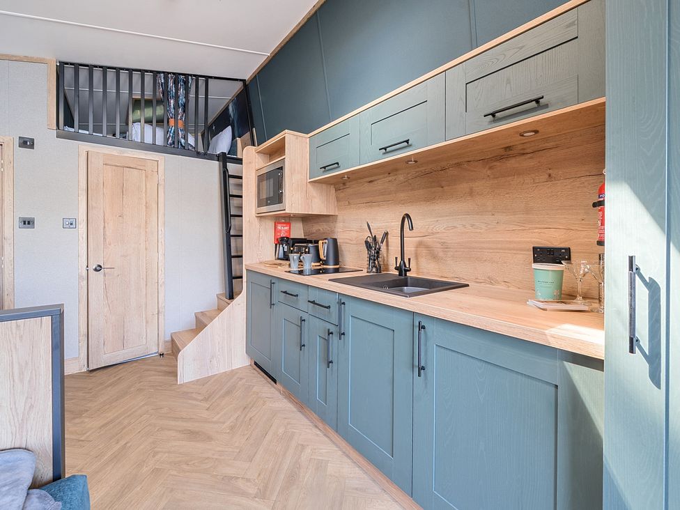 A kitchen with blue cabinets wooden countertops stairs leading to a loft area with a bed at Skylight Stargazer - Billing Aquadrome Holiday Park